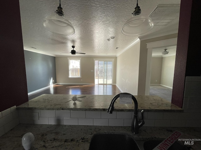 kitchen with crown molding, hanging light fixtures, stone countertops, a textured ceiling, and wood finished floors