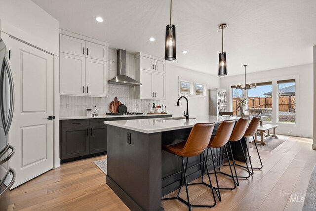 205 S Sunniva Ave, Kuna, ID 83634 - kitchen featuring wall chimney range hood, a sink, backsplash, a kitchen island with sink, and a kitchen breakfast bar