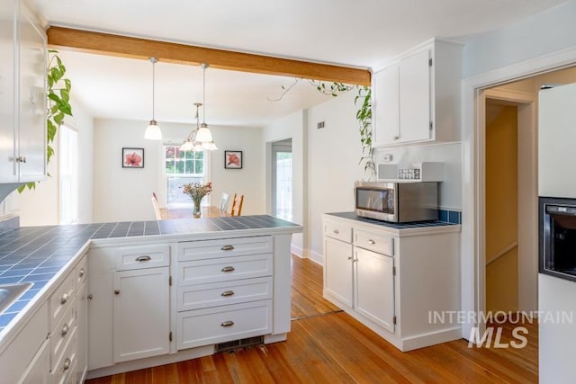 517 E C St, Moscow, ID 83843 - kitchen featuring tile counters, stainless steel microwave, a peninsula, white cabinets, and wood finished floors