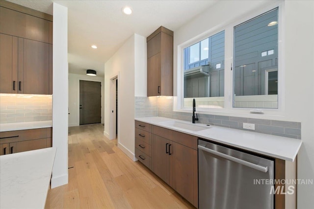 kitchen with tasteful backsplash, dishwasher, light wood-type flooring, and sink