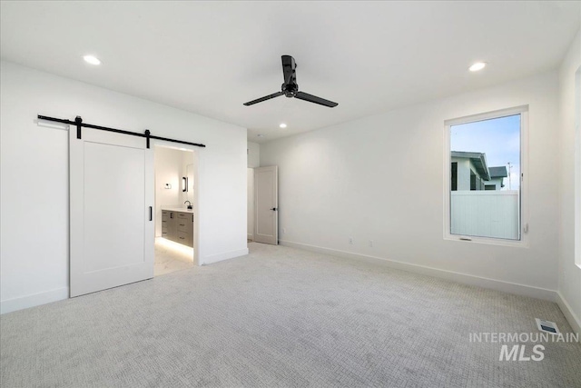 unfurnished bedroom featuring light carpet, a barn door, ensuite bathroom, and ceiling fan