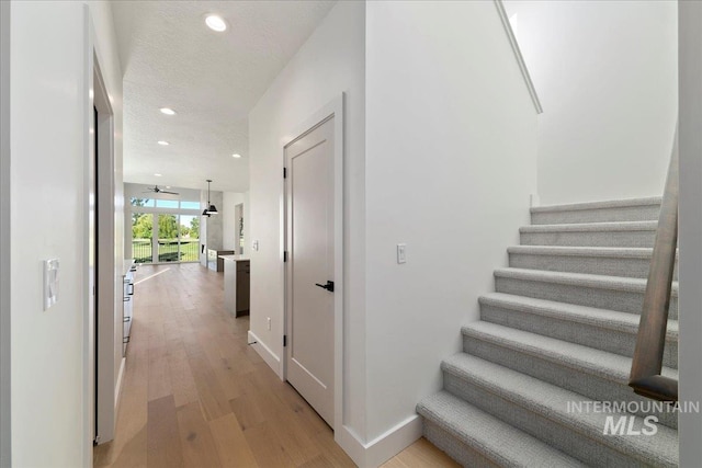 hall featuring light wood-type flooring and a textured ceiling