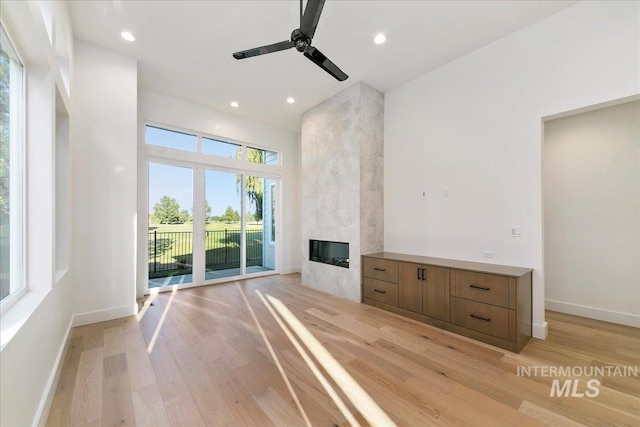 unfurnished living room with light wood-type flooring, a large fireplace, and ceiling fan