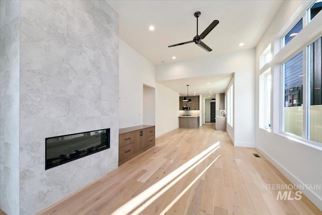 unfurnished living room with a fireplace, light hardwood / wood-style floors, ceiling fan, and a healthy amount of sunlight