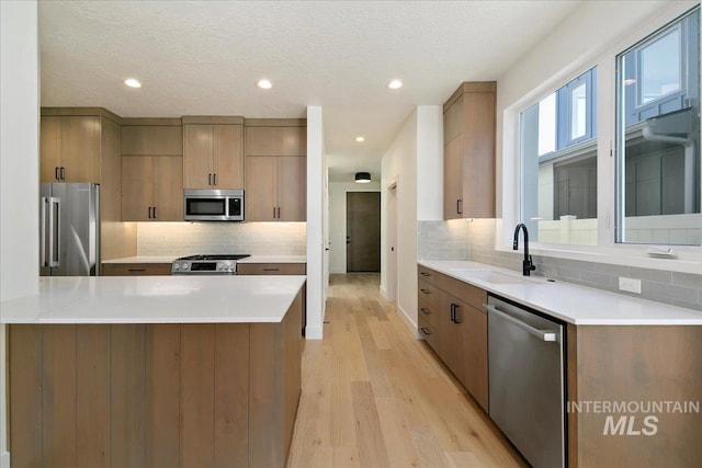 kitchen with sink, decorative backsplash, a textured ceiling, appliances with stainless steel finishes, and light hardwood / wood-style floors