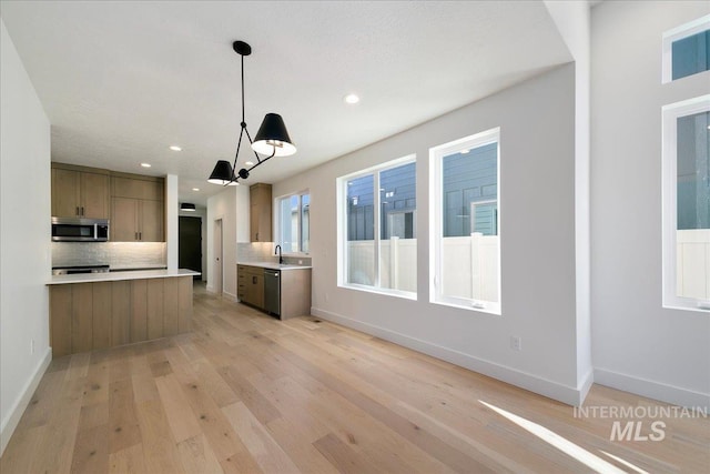 kitchen featuring backsplash, sink, light hardwood / wood-style flooring, appliances with stainless steel finishes, and decorative light fixtures