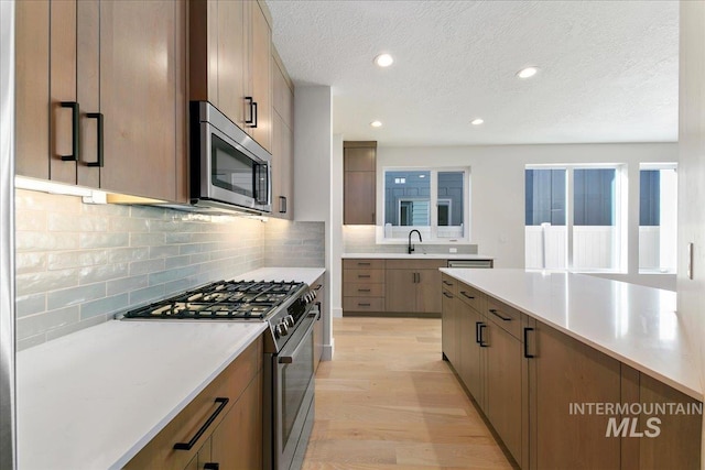 kitchen featuring sink, decorative backsplash, light wood-type flooring, a textured ceiling, and stainless steel appliances