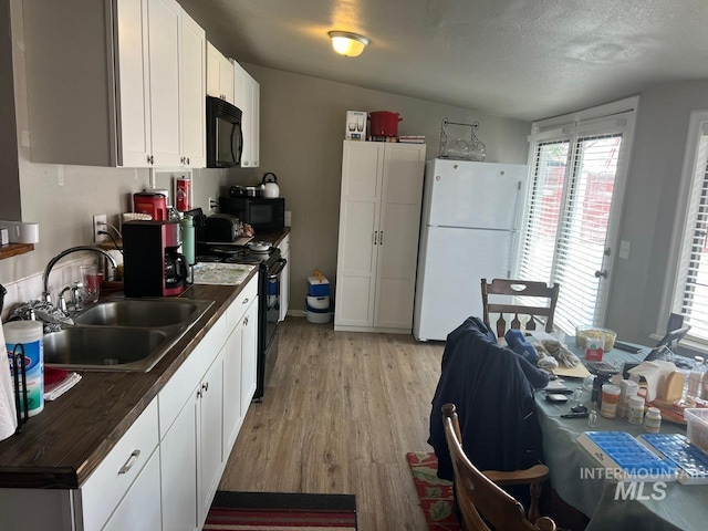 kitchen with a sink, light wood-type flooring, dark countertops, and black appliances