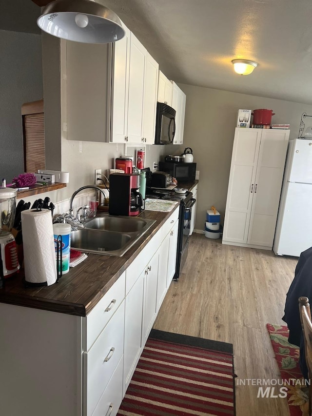 kitchen with light wood finished floors, a sink, black appliances, white cabinetry, and dark countertops