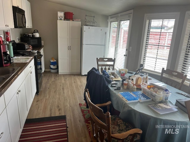 kitchen featuring a wealth of natural light, light wood-type flooring, black appliances, and white cabinetry