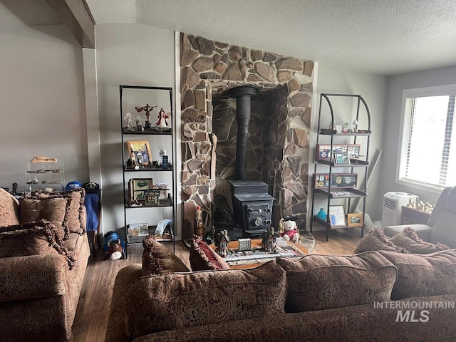 living area with lofted ceiling, a wood stove, wood finished floors, and a textured ceiling