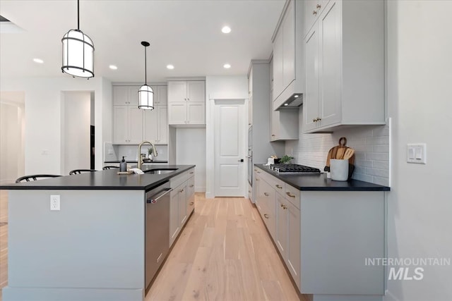 kitchen featuring light hardwood / wood-style floors, a kitchen island with sink, pendant lighting, sink, and stainless steel appliances