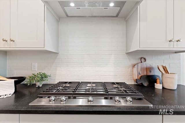 kitchen featuring stainless steel gas stovetop, ventilation hood, white cabinetry, and tasteful backsplash