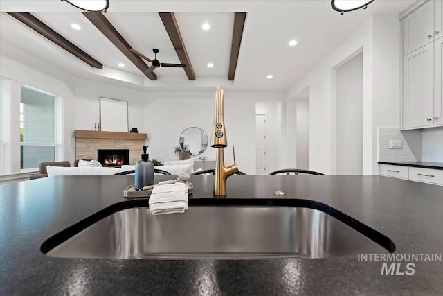 kitchen with beamed ceiling, tasteful backsplash, sink, a fireplace, and white cabinets