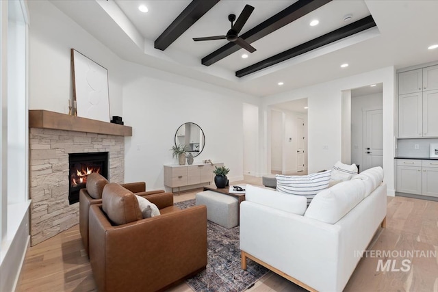 living area with light wood-style flooring, beam ceiling, recessed lighting, a ceiling fan, and a stone fireplace