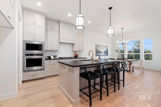 kitchen featuring sink, light hardwood / wood-style floors, an inviting chandelier, a center island with sink, and decorative light fixtures