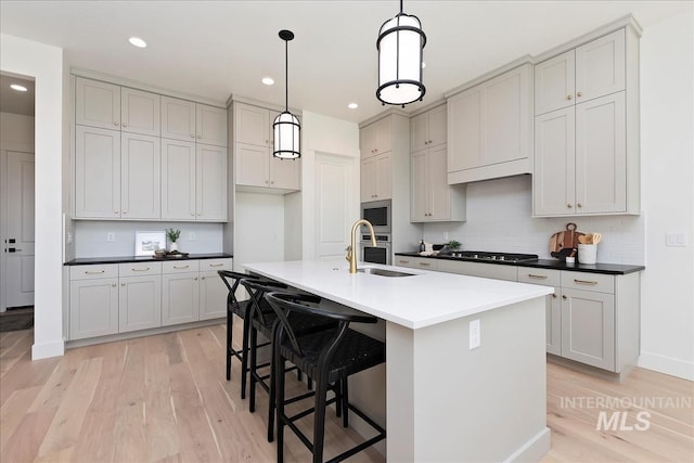 kitchen featuring stainless steel appliances, a sink, decorative backsplash, a kitchen island with sink, and light wood-style flooring