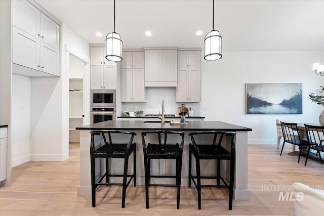 kitchen featuring appliances with stainless steel finishes, a kitchen island with sink, hanging light fixtures, and light hardwood / wood-style flooring