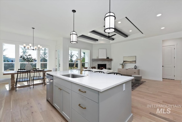 kitchen featuring recessed lighting, light countertops, a sink, a lit fireplace, and light wood-style flooring