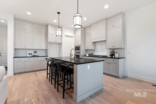 kitchen with appliances with stainless steel finishes, hanging light fixtures, a kitchen island with sink, and light hardwood / wood-style flooring