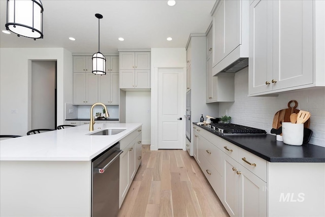 kitchen with a sink, decorative backsplash, light wood-style flooring, appliances with stainless steel finishes, and recessed lighting