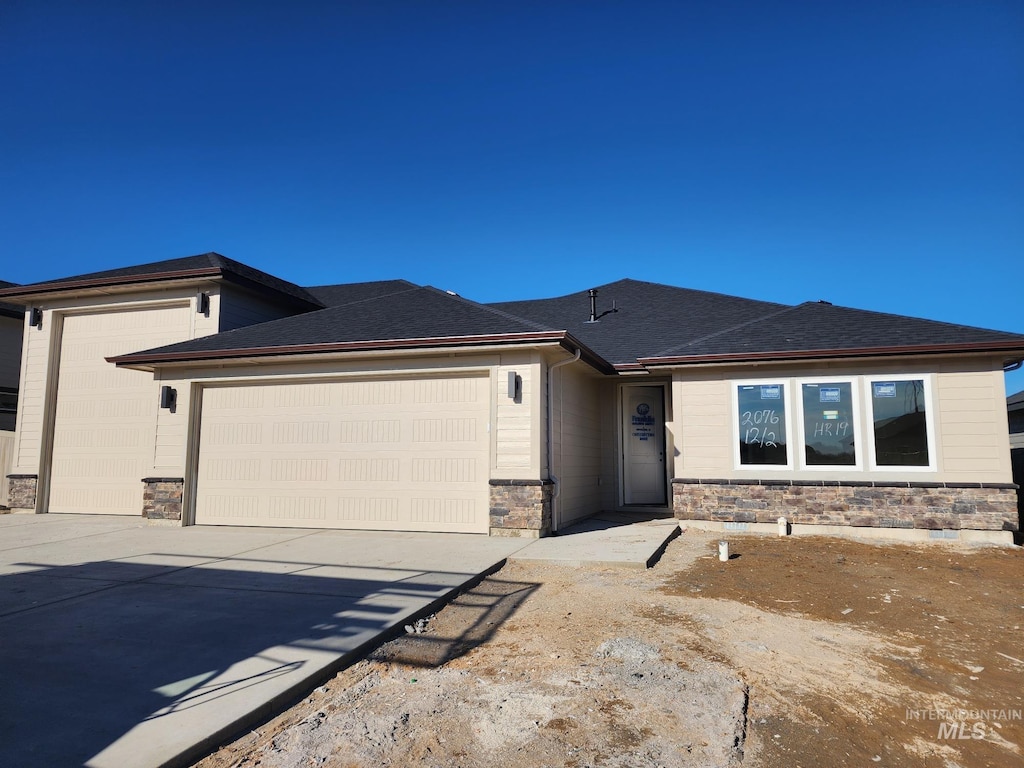 prairie-style home featuring a garage, stone siding, driveway, and a shingled roof