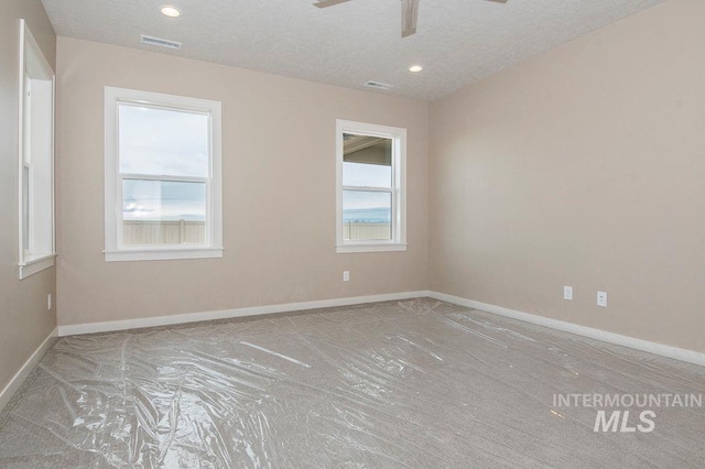 spare room featuring a textured ceiling, ceiling fan, visible vents, and baseboards