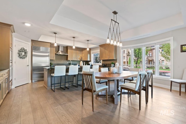 dining area with a tray ceiling, recessed lighting, and light wood-style flooring