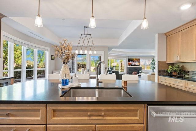 kitchen featuring dark countertops, stainless steel dishwasher, open floor plan, and a sink