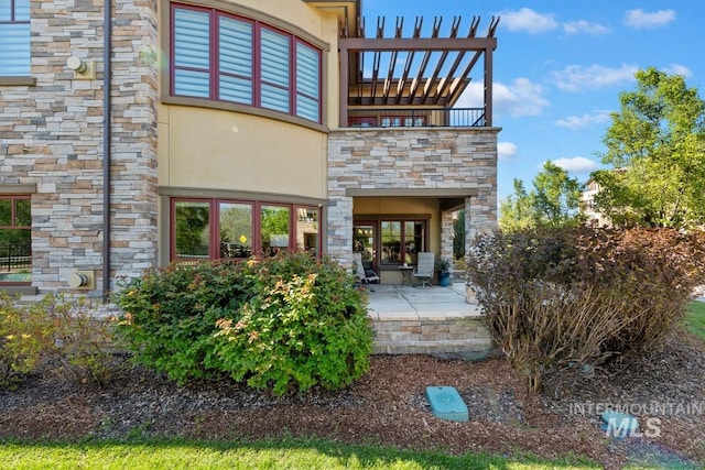 exterior space with a balcony, stone siding, a patio area, and stucco siding