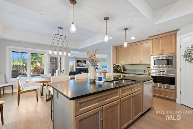kitchen with a tray ceiling, light wood finished floors, a sink, dark countertops, and appliances with stainless steel finishes