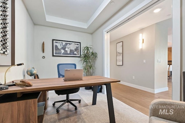 office featuring a tray ceiling, baseboards, and light wood-type flooring