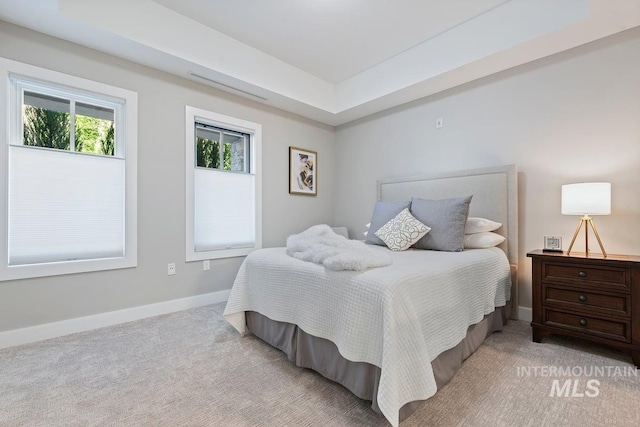 carpeted bedroom with a raised ceiling and baseboards