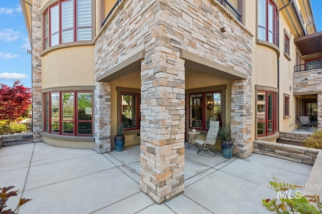 doorway to property with a patio, stucco siding, and stone siding