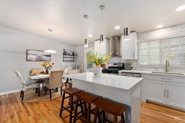 kitchen featuring wall chimney range hood, sink, decorative light fixtures, appliances with stainless steel finishes, and light hardwood / wood-style floors