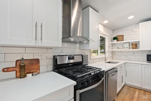 kitchen with wall chimney exhaust hood, sink, white cabinetry, appliances with stainless steel finishes, and light hardwood / wood-style floors