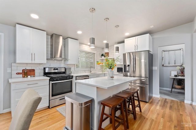 kitchen featuring a kitchen island, wall chimney exhaust hood, stainless steel appliances, pendant lighting, and white cabinets