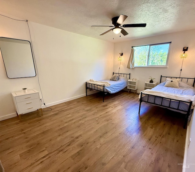 bedroom featuring ceiling fan, a textured ceiling, baseboards, and wood finished floors