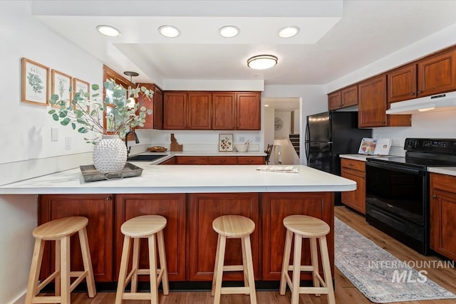 kitchen featuring light countertops, black appliances, a peninsula, and under cabinet range hood