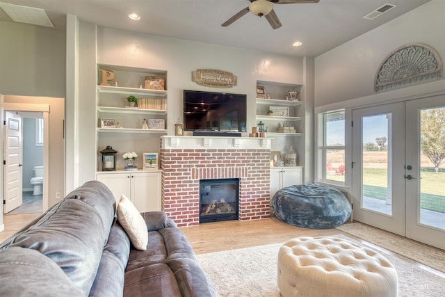 living room featuring light wood-type flooring, ceiling fan, built in features, and a brick fireplace