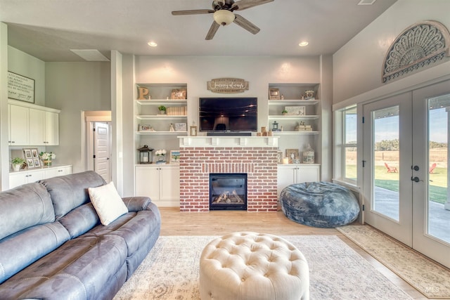 living room featuring a brick fireplace, light hardwood / wood-style flooring, built in shelves, and ceiling fan