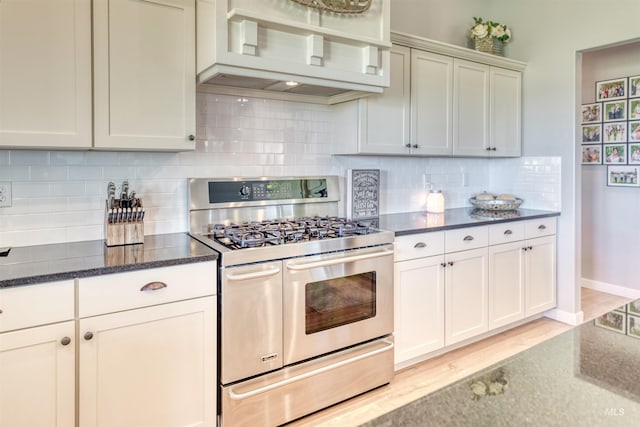 kitchen with decorative backsplash, light hardwood / wood-style floors, dark stone countertops, stainless steel gas range, and custom exhaust hood