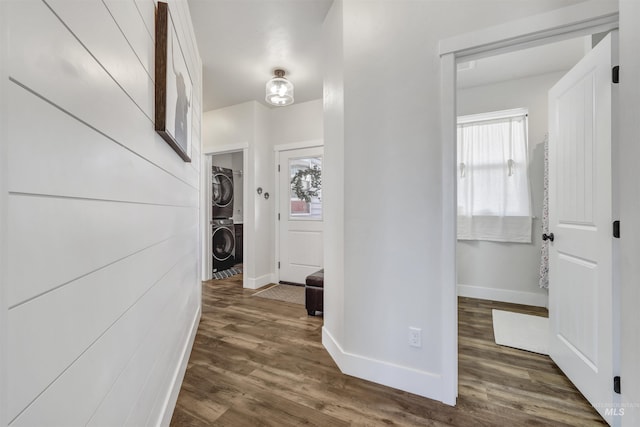 corridor featuring stacked washing maching and dryer, wood finished floors, and baseboards