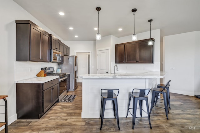 kitchen featuring dark brown cabinets, decorative backsplash, appliances with stainless steel finishes, and a kitchen breakfast bar
