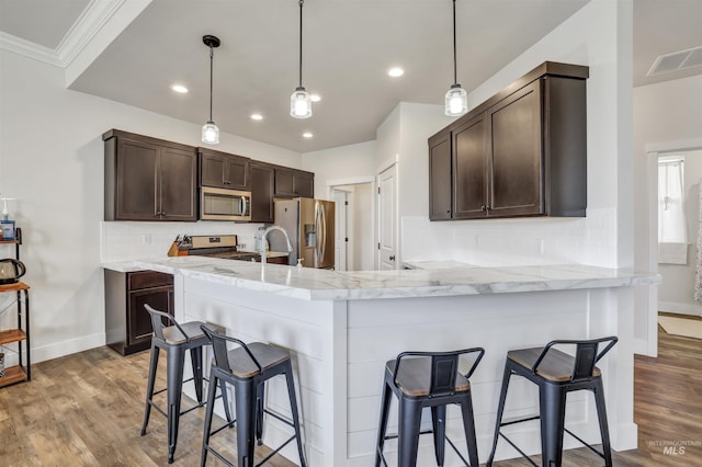 kitchen featuring dark brown cabinetry, light wood-type flooring, visible vents, a kitchen bar, and appliances with stainless steel finishes