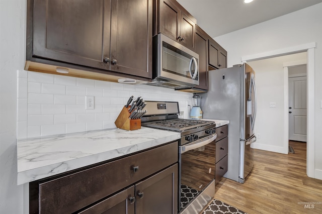 kitchen with light wood-style flooring, dark brown cabinets, light stone counters, stainless steel appliances, and decorative backsplash
