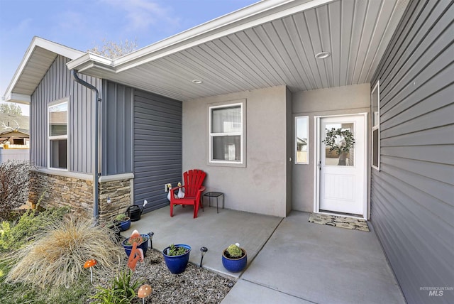 entrance to property with a patio, stucco siding, and stone siding