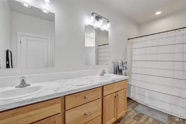 full bath featuring a sink, recessed lighting, double vanity, and wood finished floors