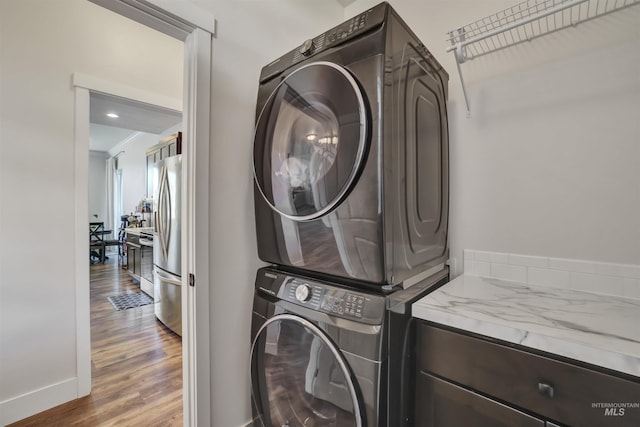 laundry room featuring stacked washing maching and dryer, laundry area, baseboards, and wood finished floors