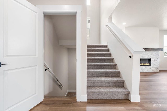 staircase with baseboards, wood finished floors, and a stone fireplace